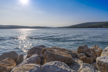 Seeufer mit großen Steinen und kleinen Hügeln in der Ferne. Kroatien