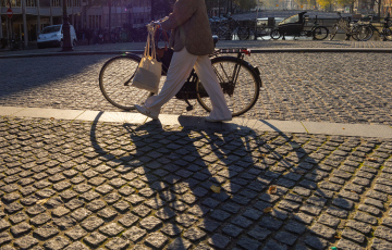 Eine Person, die an einem sonnigen Tag auf einer gepflasterten Straße Fahrrad fährt.