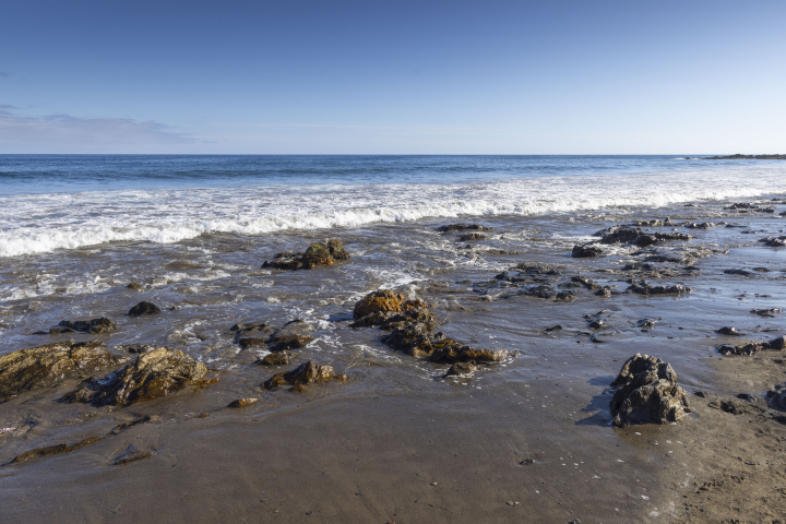 Wellen am Strand und hervorstehende flache Felsen