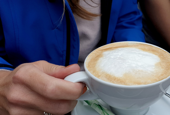 Eine Tasse Cappuccino in der Hand