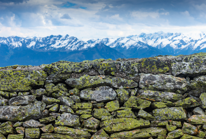 Mauer aus moosigen Steinen und Panorama der Berge